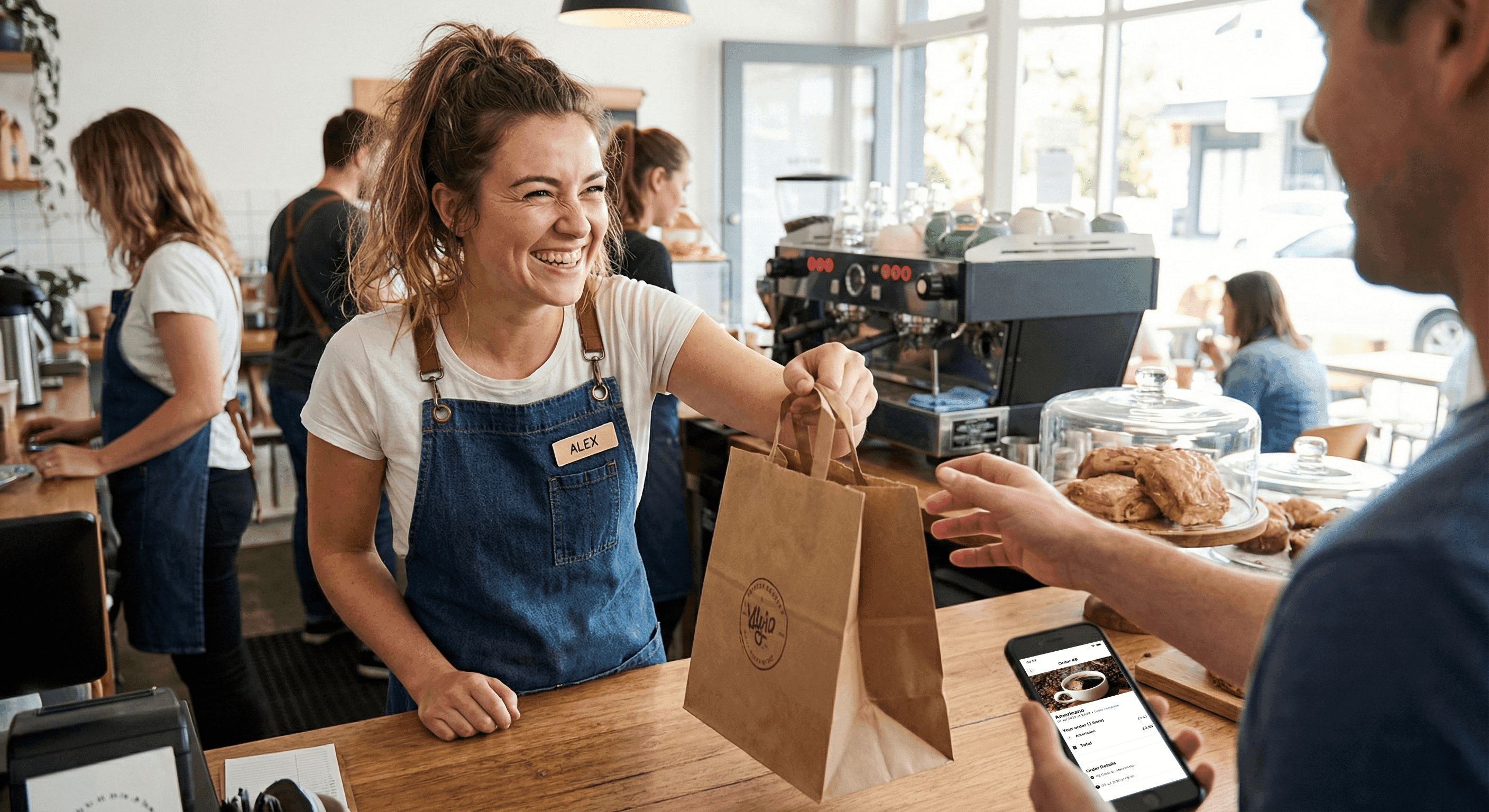 Barista handing a takeaway coffee to a customer with their phone